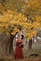 Woman in traditional red hanfu admiring the autumn leaves outdoors.