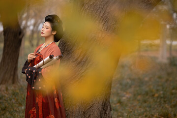 Woman in a red hanfu standing by a tree in an outdoor setting with a serene atmosphere.