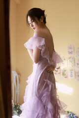 Woman in a pink ruffled dress standing in a sunlit room with floral decor.