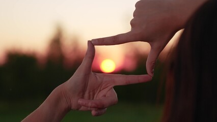 Beautiful girl gestures with her fingers to frame symbol, sun, like in movie. Hands young female director, camera operator gesture in frame at sunset in park. World seems different. Business planning