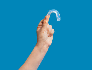 Close-up of hand holding transparent braces on blue background