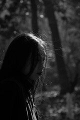 Woman in a black jacket with loose hair, standing in a serene outdoor setting.