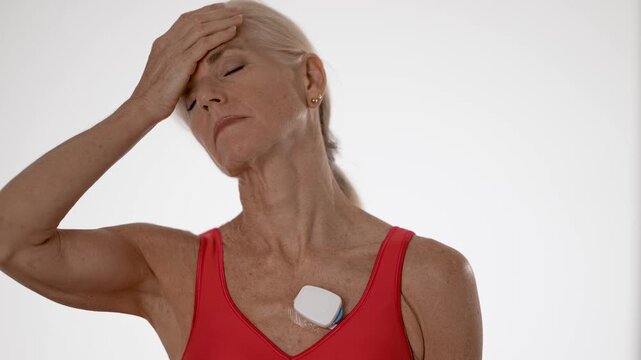 A concerned mature woman wears a heart sensor to monitor her atrial fibrillation. Isolated on a white background, she shows a proactive approach to her health.