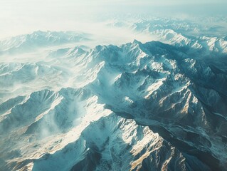 An aerial view of a winding road cutting through a snowy, hilly landscape with distant snow-capped mountains under a blue sky