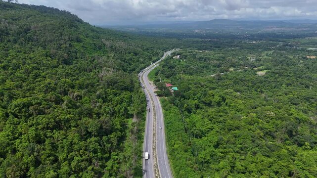 Drone footage of the aerial view of a winding road cutting through lush green forest. Scenic highway number 304 in Thailand links the Bangkok area to Nakhon Ratchasima in the northeastern region