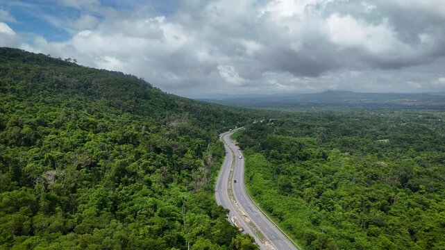 Drone footage of the aerial view of a winding road cutting through lush green forest. Scenic highway number 304 in Thailand links the Bangkok area to Nakhon Ratchasima in the northeastern region