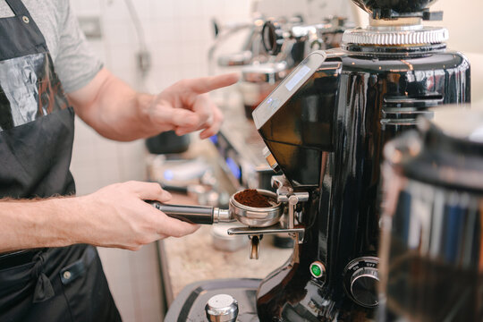 A close-up shot shows a barista's hands working the machine to measure the perfect amount of freshly ground coffee.