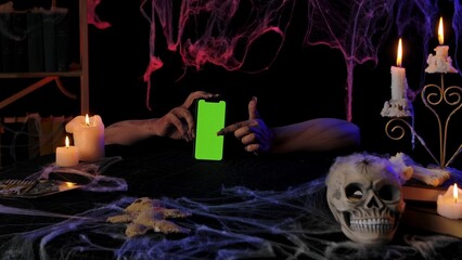 Scary zombie hands hold a smartphone with a green screen