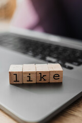 Wooden blocks spelling LIKE on laptop, concept of social media engagement, digital approval, and online interaction