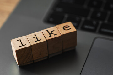 Wooden blocks spelling LIKE on laptop, concept of social media engagement, digital approval, and online interaction