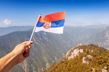 Hand holding a small Serbian national flag flying proudly over a vast mountainous landscape, symbolizing patriotism and travel