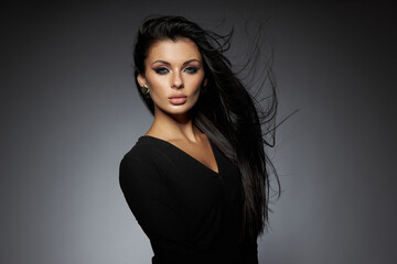confident model stands with her hair flowing in the air, showcasing her unique style and makeup in a studio setting during the evening hours. She exudes elegance and poise