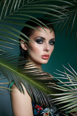 scene captures a model with striking makeup posing between lush green palm leaves. soft lighting enhances the models features, creating a captivating atmosphere for the shoot