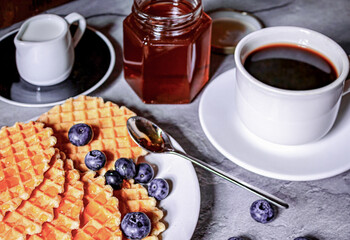 Breakfast on the table, a cup of coffee and waffles, blueberries and honey
