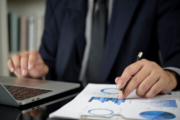 Obraz premium Businessman analyzing financial data report at office desk. Man hand pointing pencil at chart, graph for investment planning, audit. Business performance, market analysis, and strategy concept.