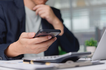 Businessman thinking, analyzing financial data on smartphone at office desk. Man using mobile app for investment planning, stock market research. Business technology, finance, and strategy concept.