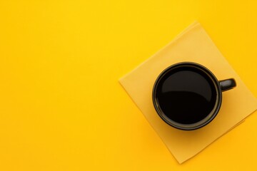 Coffee cup on Yellow Background: A single, stylish black coffee cup sits atop a square paper napkin on a vibrant yellow background.