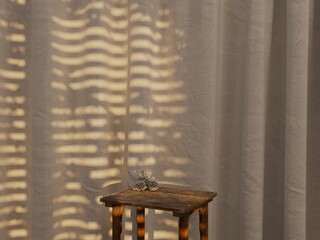 Symmetric product display table with pinecone and blinds shadow on sheer curtain.