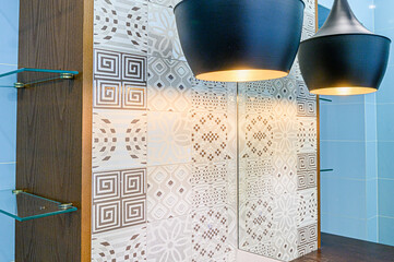 modern bathroom features patterned tiles, black pendant lights, a wooden cabinet with glass shelves, and light blue wall tiles