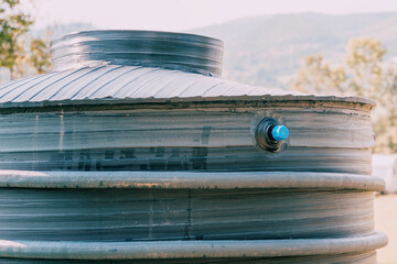 Black plastic water tank capturing and storing rainwater for conservation in a rural setting, promoting sustainable water use