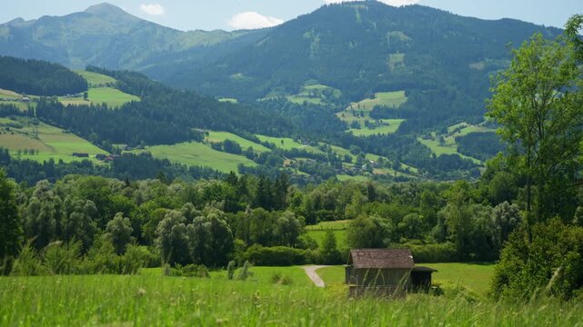 A stunning summer landscape of a mountain valley in the Austrian Alps. A traditional wooden hay barn sits on a green meadow, adding to the idyllic rural scenery for travel or agriculture themes.