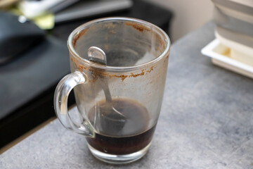 A glass cup containing leftover coffee sits on a grey countertop. The cup shows signs of use with coffee stains along the rim, representing daily routines and coffee culture.