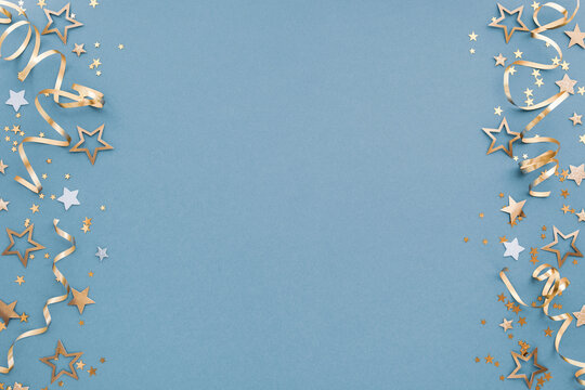 Christmas, New Year or birthday festive blue border background top view. Celebration composition with golden confetti stars and serpentine party streamers.