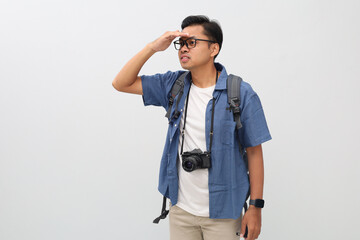 Side view of young man traveler wearing casual clothes, backpack, camera hanging around his neck, looking far ahead, isolated on white background, vacation or travel adventure concept.