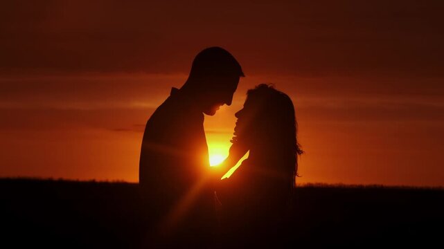 Silhouettes of a man and woman against the backdrop of sunset, lovers in an intimate moment. Concept love story. Super slow-motion shot.