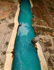 High-angle view of a vibrant turquoise river channel carved through a landscape of light beige and brown earth
