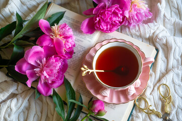 Delicate peony flowers and a cup of aromatic tea on the table.