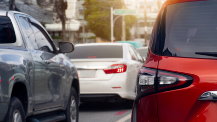 Rear side of luxury orange car driving on the asphalt road. Cars in traffic jam on a city street. Blurred background other cars in the city with trees.