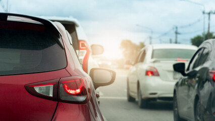 Fototapeta premium Rear side of red car with turn on brake light. Traffic jam on the road. Many cars stopped to cross the intersection. Blurred background of electric pole and trees and other car driving on the road.