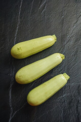 Bright, fresh yellow zucchini on a dark, textured background. Top shot, contrasting light.