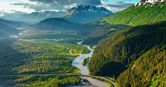 Beautiful green pine tree woods covering the mountains and vast valley. Branching river flows in the valley. Grey cloudscape hang in the sky over the rocks. Alaska, USA.