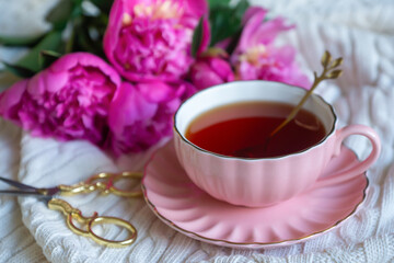 Delicate peony flowers and a cup of aromatic tea on the table.