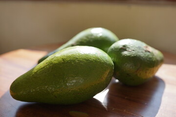 Fresh Hass avocados on a wooden surface with natural sunlight casting shadows