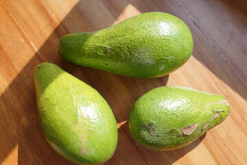 Three fresh, ripe avocados on a wooden surface, showcasing their healthy green skin and natural texture