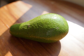 Fresh green avocado fruit on a wooden table bathed in sunlight