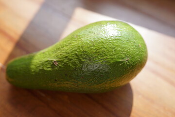 A single, ripe avocado resting on a wooden surface, bathed in natural sunlight