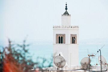 White islamic minaret tower of mosque of sidi bou said city against Mediterranean sea and sky on background - religious symbol. Tunisia