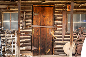 Antique wooden door and glass paned window closed with rustic old mining work tools on the weathered wood wall. Historic house building entrance for architecture background
