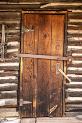 Antique wooden door closed with rustic old mining work tools on the weathered wood wall. Historic house building entrance for architecture background