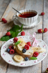For breakfast, there are toasts with fruits and berries and a cup of aromatic tea on the table.