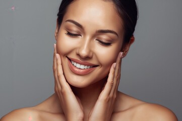 Portrait of smiling young woman gently touching her face with closed eyes showcasing healthy skin on neutral grey background for beauty and skincare concepts