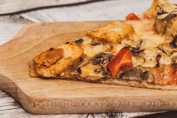 A close-up of a delicious slice of pizza topped with chicken, mushrooms, and red bell peppers, presented on a wooden cutting board. Perfect for food-related content.