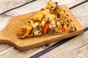 A delicious slice of pizza topped with mushrooms, red peppers, and chicken, served on a wooden board, perfect for a casual meal or party setting.