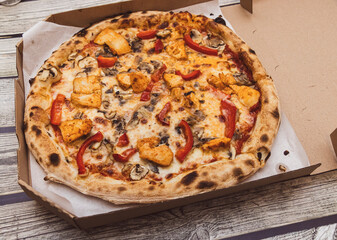 Freshly baked pizza topped with chicken, mushrooms, and red peppers, served in an open cardboard box, perfect for a casual meal or gathering with friends.