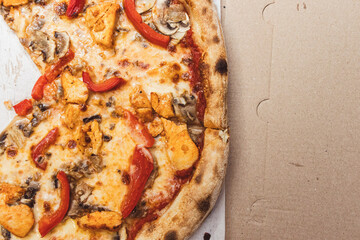 Delicious slice of pizza topped with chicken, mushrooms, and red pepper on a cardboard pizza box, showcasing a casual dining experience.