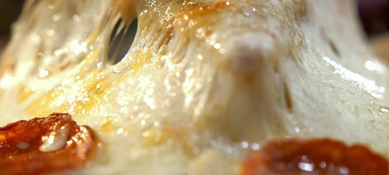 Macro shot of a person taking a slice of hot pepperoni pizza with delicious melted mozzarella cheese stretching in slow motion, showing a perfect appetizing cheese pull from the italian food